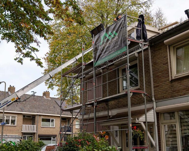Het team van Wijdekkendaken werkt aan de renovatie van een woningdak met steigers en een daklift naast een bakstenen huis.